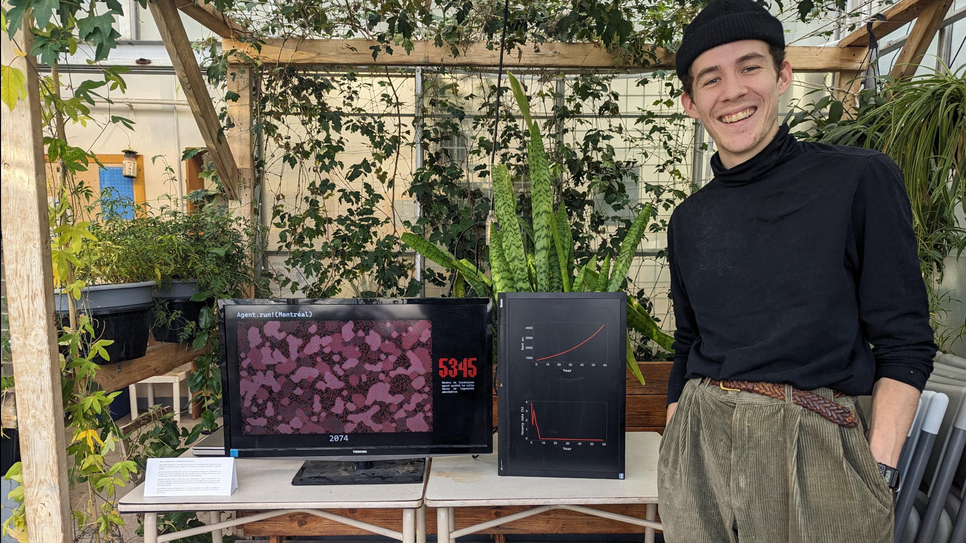 Image of Lucien in front of a dual screen installation simulating the housing crisis in montreal